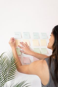 a woman is painting the wall with pastel swatches and palm leaves in front of her