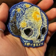 a hand holding a small patch with a painting on it's face in the shape of a skull