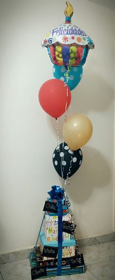 a bunch of balloons that are on top of some books and presents in front of a wall