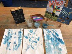 three pieces of paper with blue and white paint sitting on top of a wooden table