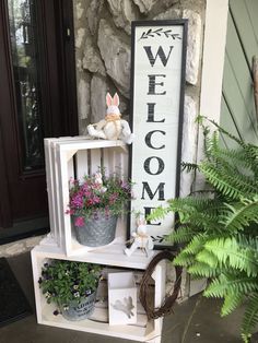 a welcome sign sitting on top of a white shelf filled with potted plants and flowers