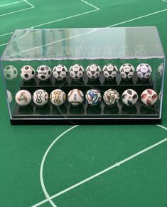 a display case holds twelve soccer balls on a green surface with white lines in the background