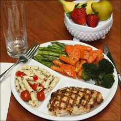 a white plate topped with meat and veggies next to a bowl of fruit