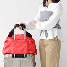 A woman standing with a grey suitcase with a large red bag through the handle she holds. Functional Foldable Travel Accessories For On-the-go, Versatile Travel Bag With Zipper Pocket For Overnight Trips, Versatile Travel Bag With Zipper For Overnight Trips, Travel Bag With Zipper Pocket For Overnight Trips, Functional Foldable Travel Bag For Daily Use, Functional Foldable Travel Bag For Outdoor Activities, Multifunctional Packable Travel Bag For Outdoor Activities, Practical Packable Travel Accessories For On-the-go, Packable Multifunctional Travel Bag For Outdoor Activities