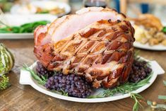 a ham is sitting on a plate with grapes and other food items around the table