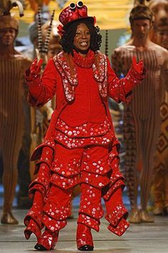 a woman in a red dress and headdress on the runway at a fashion show