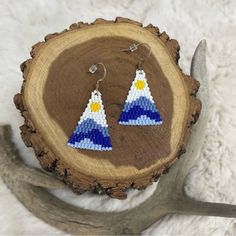 a pair of beaded earrings sitting on top of a piece of wood next to a deer's antler