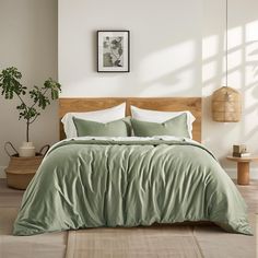 a bed with green sheets and pillows in a white room next to a potted plant