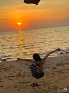 a woman sitting in a hammock on the beach at sunset with her arms outstretched