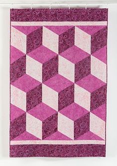 a pink and white quilt hanging on a wall