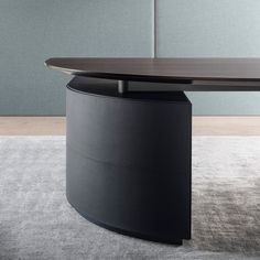 an oval shaped table with a black base on carpeted floor next to gray wall