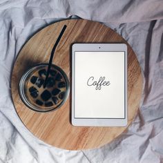 a tablet sitting on top of a wooden table next to a cup of coffee and a drink