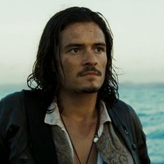 a man with long hair standing in front of the ocean