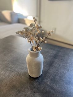 a white vase filled with flowers on top of a wooden table next to a bed