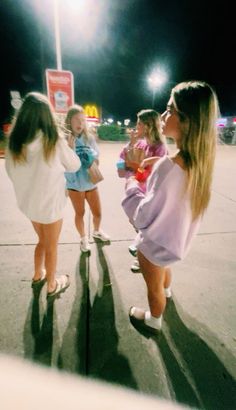 three girls are standing on the sidewalk at night