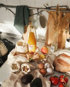 an assortment of food is displayed on a kitchen counter with bread, eggs, tomatoes and other ingredients