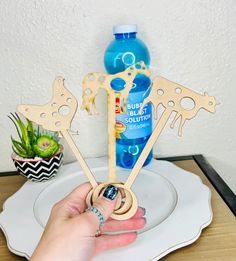 a person holding up some wooden cutouts on a plate with a water bottle in the background