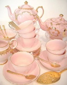 a pink tea set with gold trimmings and matching cups, saucers, and spoons