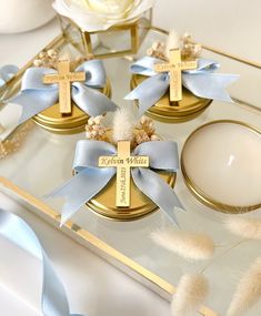 three gold candles with blue ribbons around them and a white rose on the table next to it