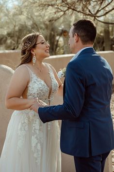 a bride and groom smile at each other while standing in front of a stone wall