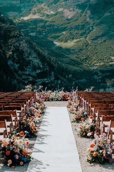 an outdoor ceremony setup with wooden chairs and flower arrangements on the aisle, overlooking mountains