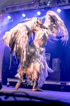 a woman dressed in white is dancing on stage with feathers and chains around her body