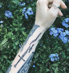 a person with a tattoo on their arm holding a cell phone in front of blue flowers