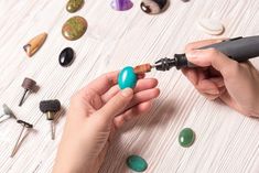 two hands are working on an object with various tools and stones around them, including pens