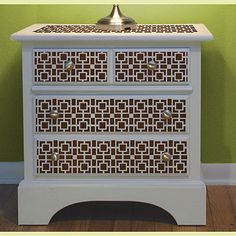 a white cabinet with two drawers and a lamp on top of the drawer, against a green wall