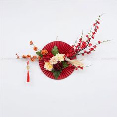 a red paper plate with flowers and branches on the top is hanging from a string