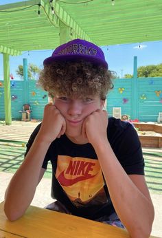 a young boy sitting at a table with his hands on his face while wearing a nike hat