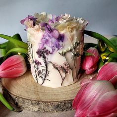 there is a cake with flowers on it next to pink tulips and green leaves