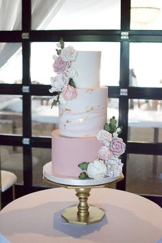 a three tiered cake with pink and white flowers on the top is sitting on a table