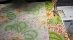 the sewing machine is next to the flowered tablecloth on the bed sheet that's being sewn