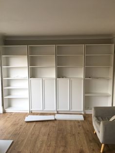 an empty living room with white bookcases and wood flooring in the middle