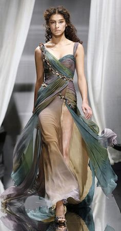 a woman is walking down the runway wearing a dress with sheer draping on it