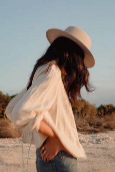 a woman in a hat is standing on the beach with her back to the camera