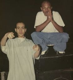 two men sitting on top of suitcases with their hands in the air and one man standing behind them