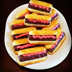 a white plate topped with mini sandwiches covered in chocolate and pink frosted icing