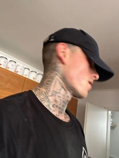 a man with tattoos on his neck wearing a black shirt and hat in a kitchen