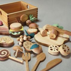 wooden toys are arranged on the floor in front of a box with spoons and other items