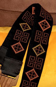 a pair of black and gold knitted guitar straps on a yellow surface with an orange background