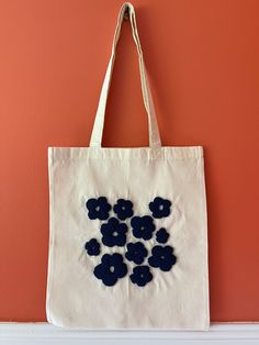 a white tote bag with blue flowers on it hanging from the wall next to an orange wall