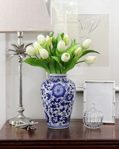 a blue and white vase with flowers in it sitting on a table next to a lamp