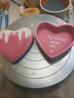 two heart shaped cookies sitting on top of a metal tray next to paint brushes and paints