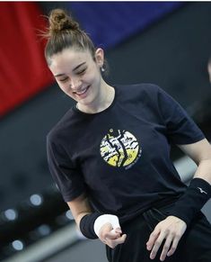 a woman holding a white object in her right hand and wearing a black shirt with an eagle on it