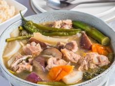 a bowl filled with meat and vegetables on top of a table next to some rice