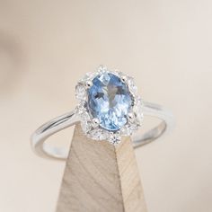 an oval blue topaz ring sits atop a wooden stand with a diamond center in the middle