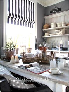 a kitchen counter topped with lots of clutter and candles next to a window covered in black and white striped blinds