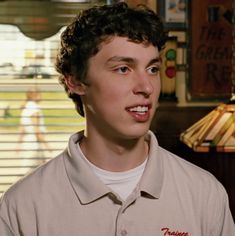 a young man wearing a polo shirt in front of a table with a lamp on it